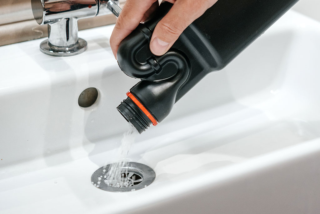Removal of blockage in the sink, the hand of a man with a bottle of a special remedy with granules. Clean the blockages in the bathroom with chemicals.